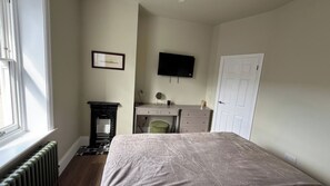Ein Schlafzimmer mit Bett, Schreibtisch, Stuhl, Heizkörper, Fernseher und einer Tür.