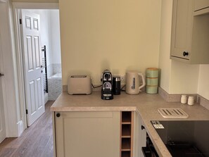 Een keuken met een broodrooster, koffiezetapparaat, waterkoker en een groene mok op het aanrecht.