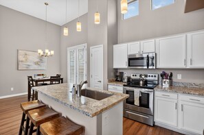 A kitchen with white cabinets, a granite countertop, stainless steel appliances, and a dining area with wooden chairs and a table. - NEW! Scottsdale Basecamp with Prime Golf Access (Scottsdale)