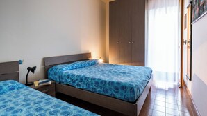 Een slaapkamer met twee bedden, een kledingkast, een nachtkastje en een raam met gordijnen.