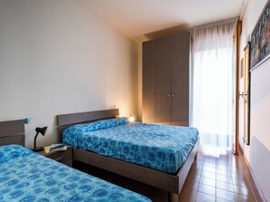 Ein Schlafzimmer mit zwei Betten, einem Kleiderschrank, einem Nachttisch und einem Fenster mit Vorhängen.
