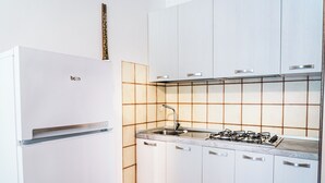 Een moderne keuken met een witte koelkast, een gasfornuis en witte kasten.