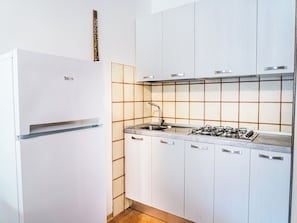 Een moderne keuken met een witte koelkast, een gasfornuis en witte kasten.