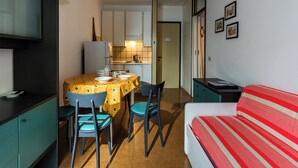 Een kleine kamer met een eettafel, stoelen, een bed en een kitchenette.