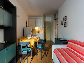Een kleine kamer met een eettafel, stoelen, een bed en een kitchenette.
