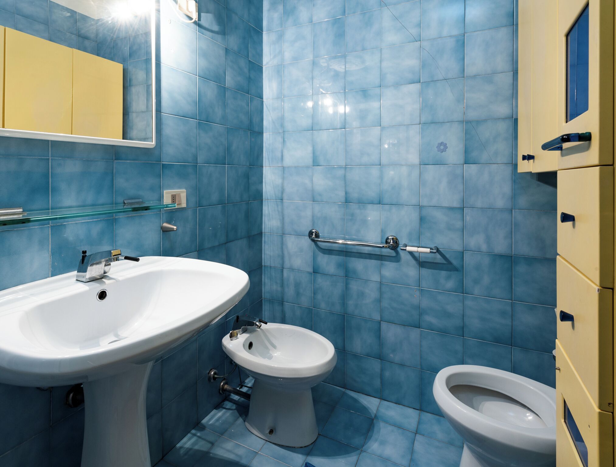 A bathroom with blue tiles, a white sink, a toilet, and a bidet.