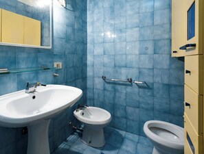 Ein Badezimmer mit blauen Fliesen, einem weißen Waschbecken, einer Toilette und einem Bidet.