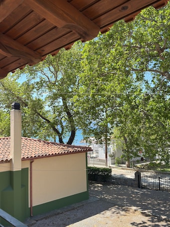 A building with a tiled roof, a green and beige facade, and a view of trees and a body of water in the background.. Apartment 'Kyriakos' with Mountain View, Wi-Fi, and Air Conditioning
