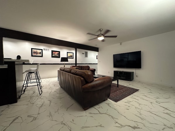 A modern living room with a sofa, a bar area, a ceiling fan, and a flat-screen TV.