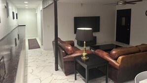 Una sala de estar moderna con un sofá de cuero, una mesa con una lámpara, un televisor de pantalla plana y un ventilador de techo.