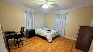 Een slaapkamer met een bed, een bureau, een stoel, een plafondventilator en een kledingkast.
