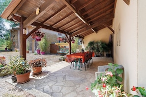 A covered patio with a stone floor, wooden ceiling, and a table with chairs.