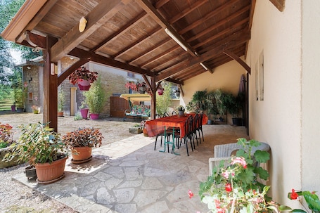 A covered patio with a stone floor, wooden ceiling, and a table with chairs.. “Jonquille” Guest Room with Shared Terrace, Garden, and Wi-Fi