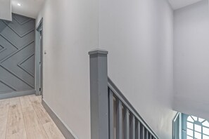 A modern interior with a wooden floor, a grey chevron-patterned door, and a staircase with a grey railing.