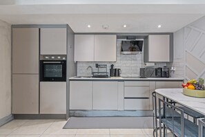 A modern kitchen with a built-in oven, a sink, and a countertop with a fruit bowl. - Stylish | Modern 3 Bed in Holland Park - Central London (Greater London)
