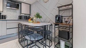 Eine moderne Küche mit weißem Marmorbelag, schwarzen Stühlen, einer Kaffeemaschine und einer Uhr an der Wand.