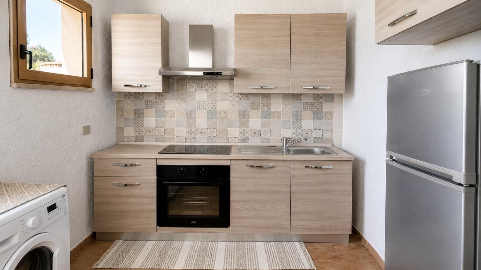 Eine kompakte Küche mit Einbauofen, Edelstahlkühlschrank und Fliesenrückwand.