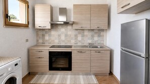Eine kompakte Küche mit Einbauofen, Edelstahlkühlschrank und Fliesenrückwand.