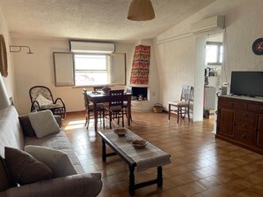 Ein Wohnzimmer mit einer Couch, einem Holztisch, einem Esstisch mit Stühlen, einem Kamin und einem Fernseher auf einer Kommode.