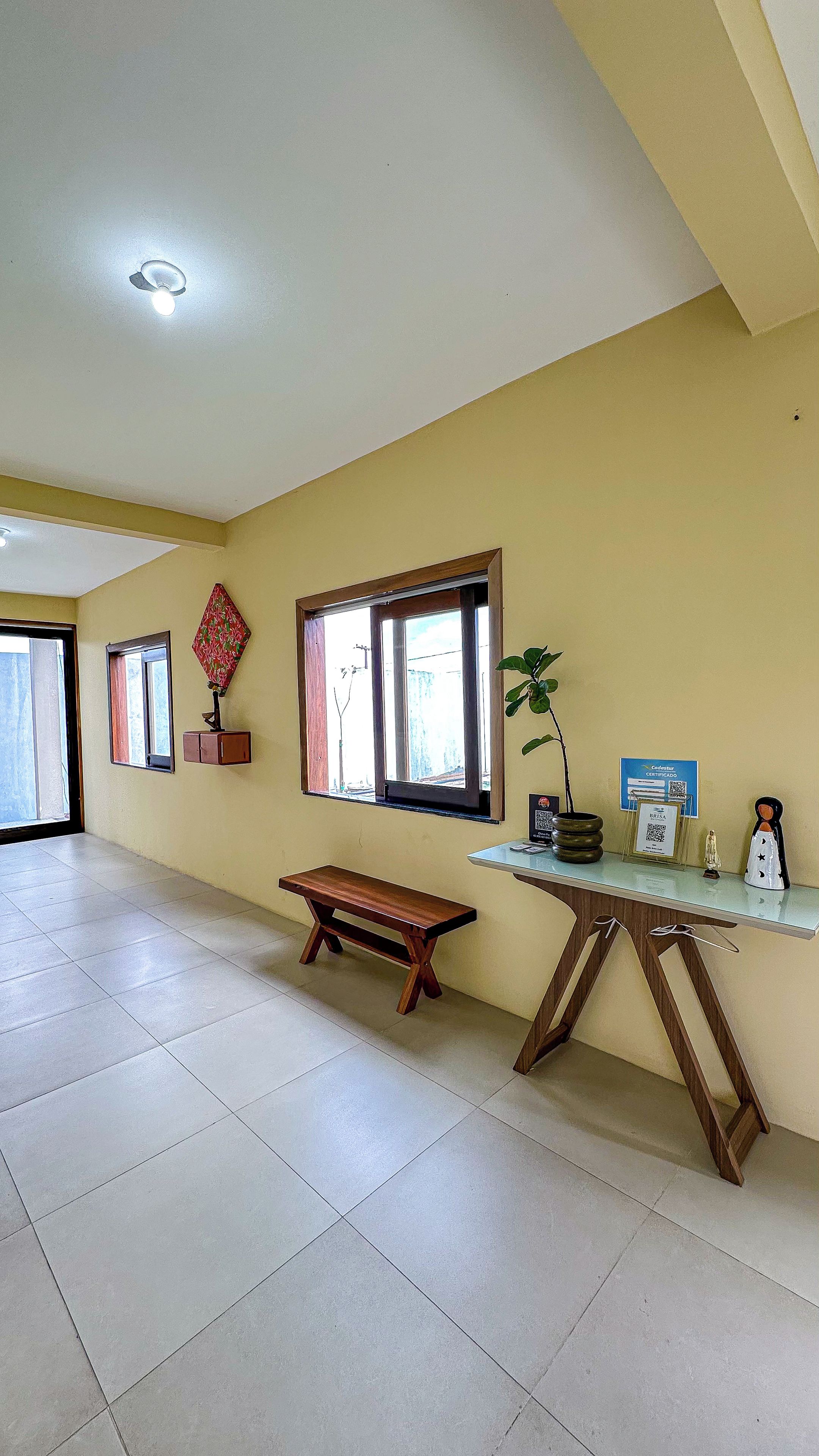 A room with a bench, a table with a plant, a window, and a certificate on the wall.