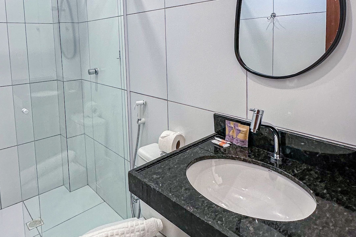 Un baño con cabina de ducha de vidrio, un inodoro blanco, un lavamanos con encimera negra y un espejo con marco de madera.