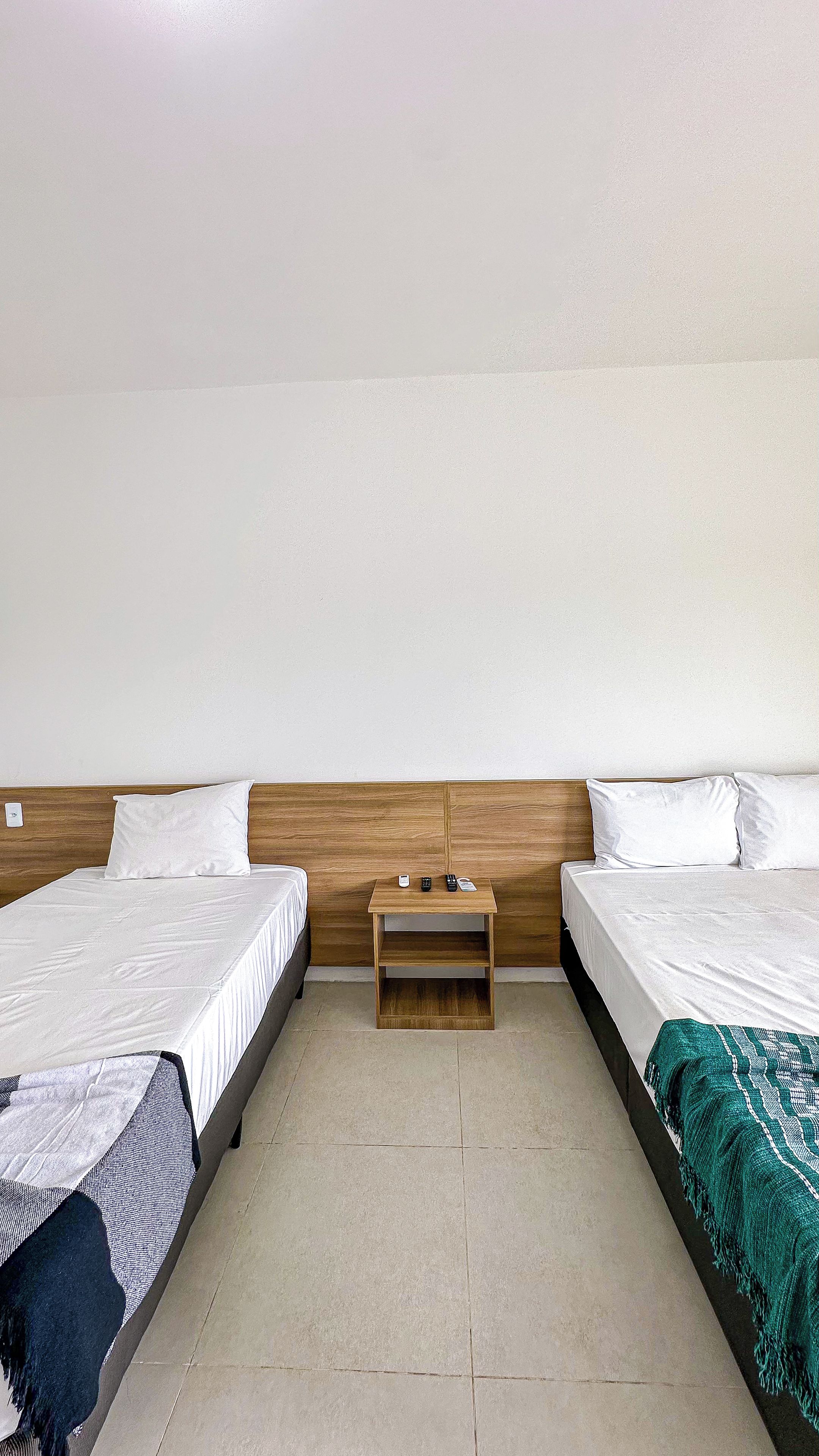 A room with two beds, a wooden nightstand, and a green blanket.