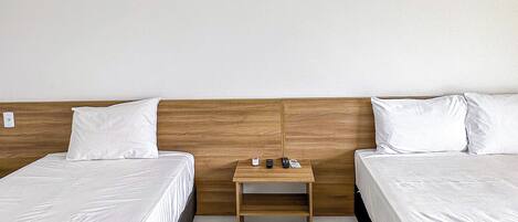 A room with two beds, a wooden nightstand, and a green blanket.