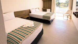 Habitación de hotel con dos camas, televisión, una silla y balcón con cortinas.