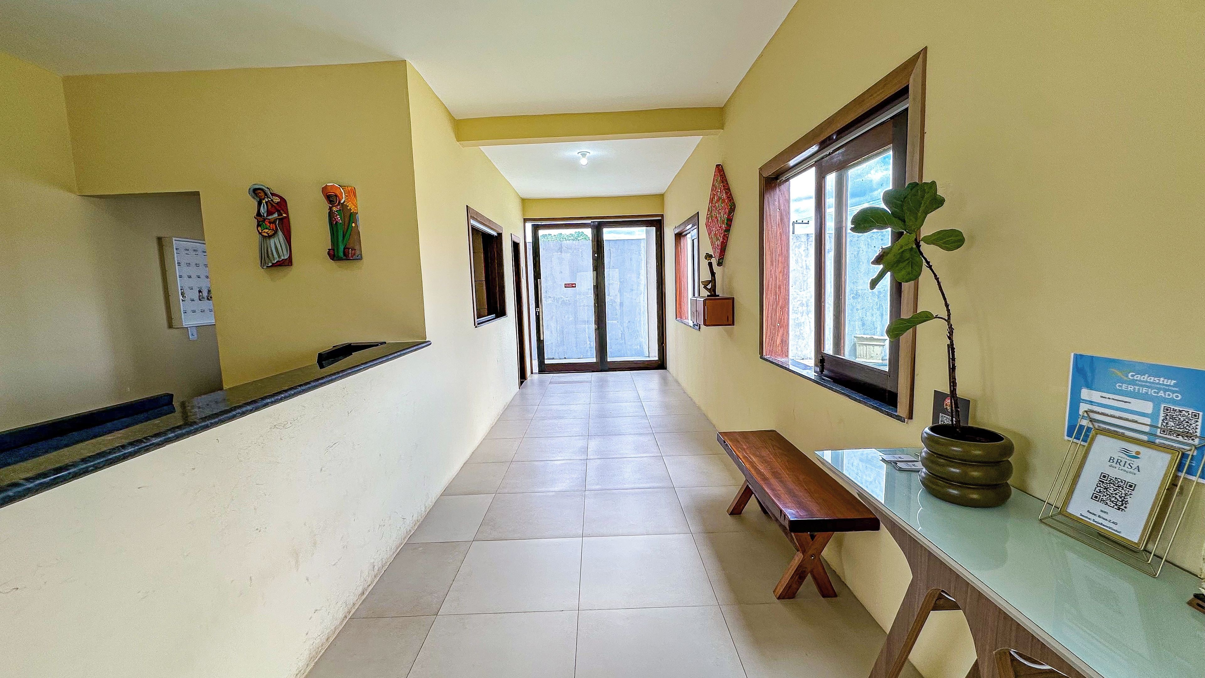 A hotel corridor with a bench, a reception desk, and a window with a plant.