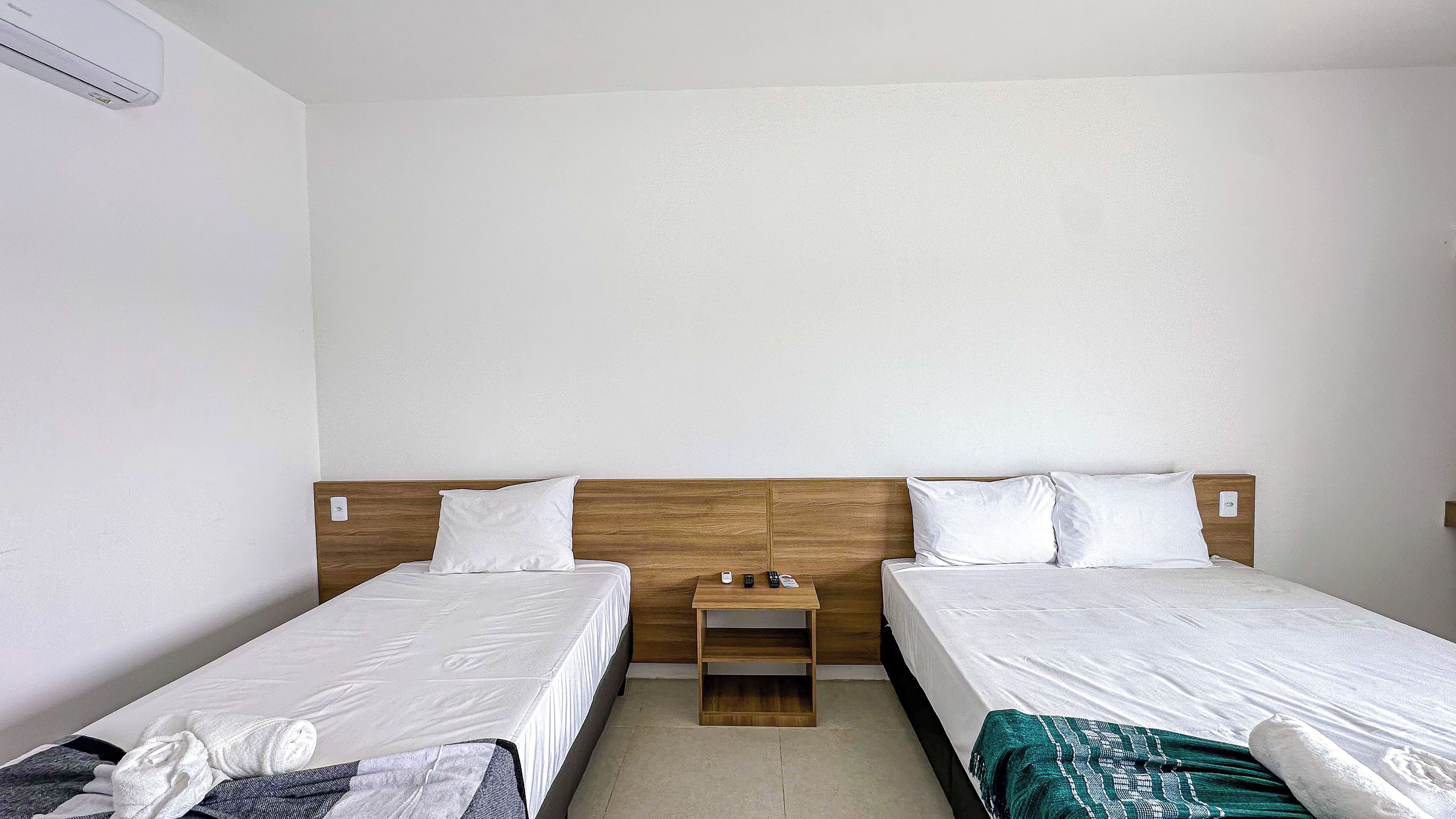 Une chambre d’hôtel avec deux lits simples, une tête de lit en bois, une petite table de chevet et un climatiseur fixé au mur.