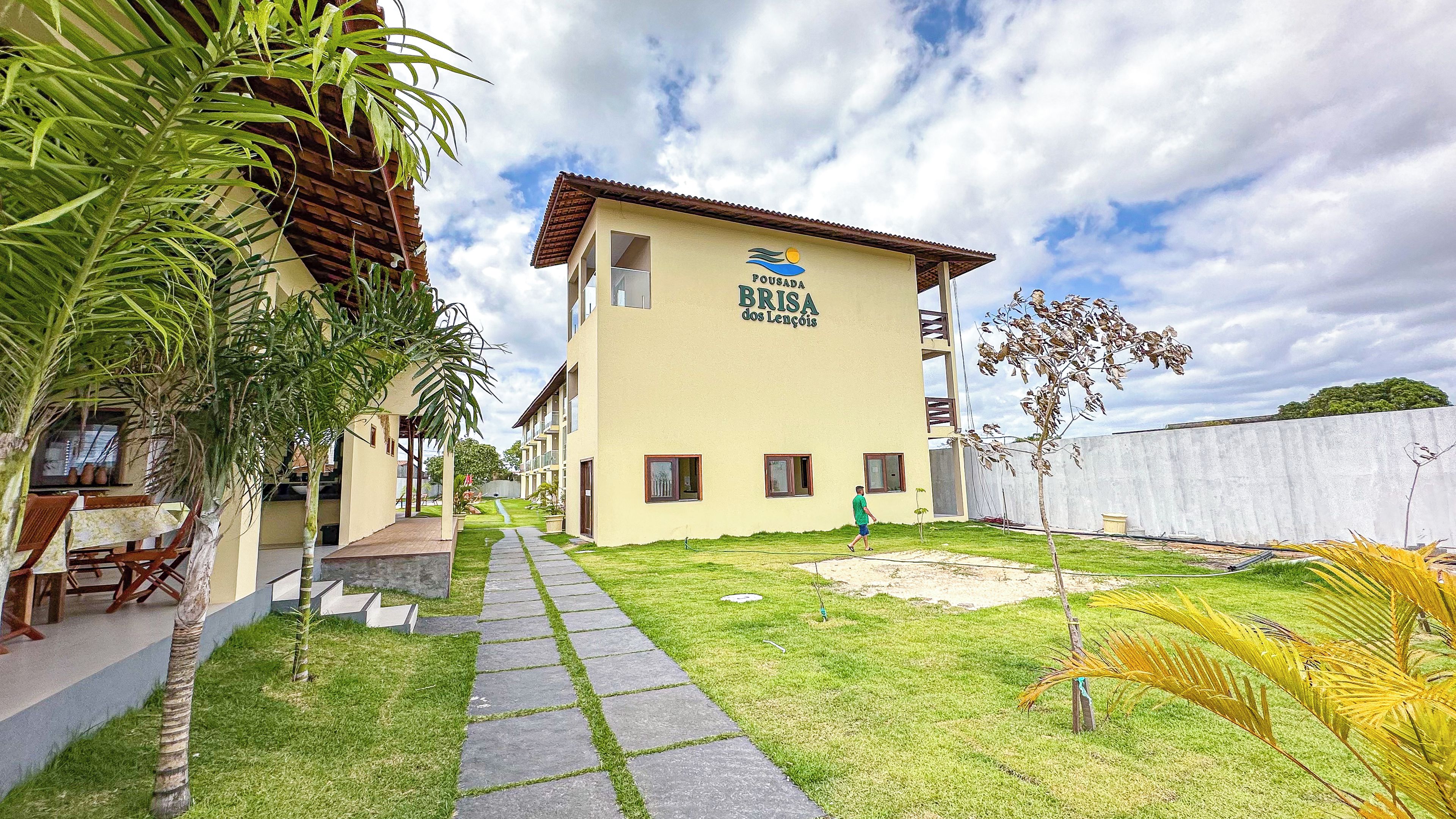 A building with a sign reading 'Pousada Brisa dos Lençóis' with a pathway leading to the entrance.