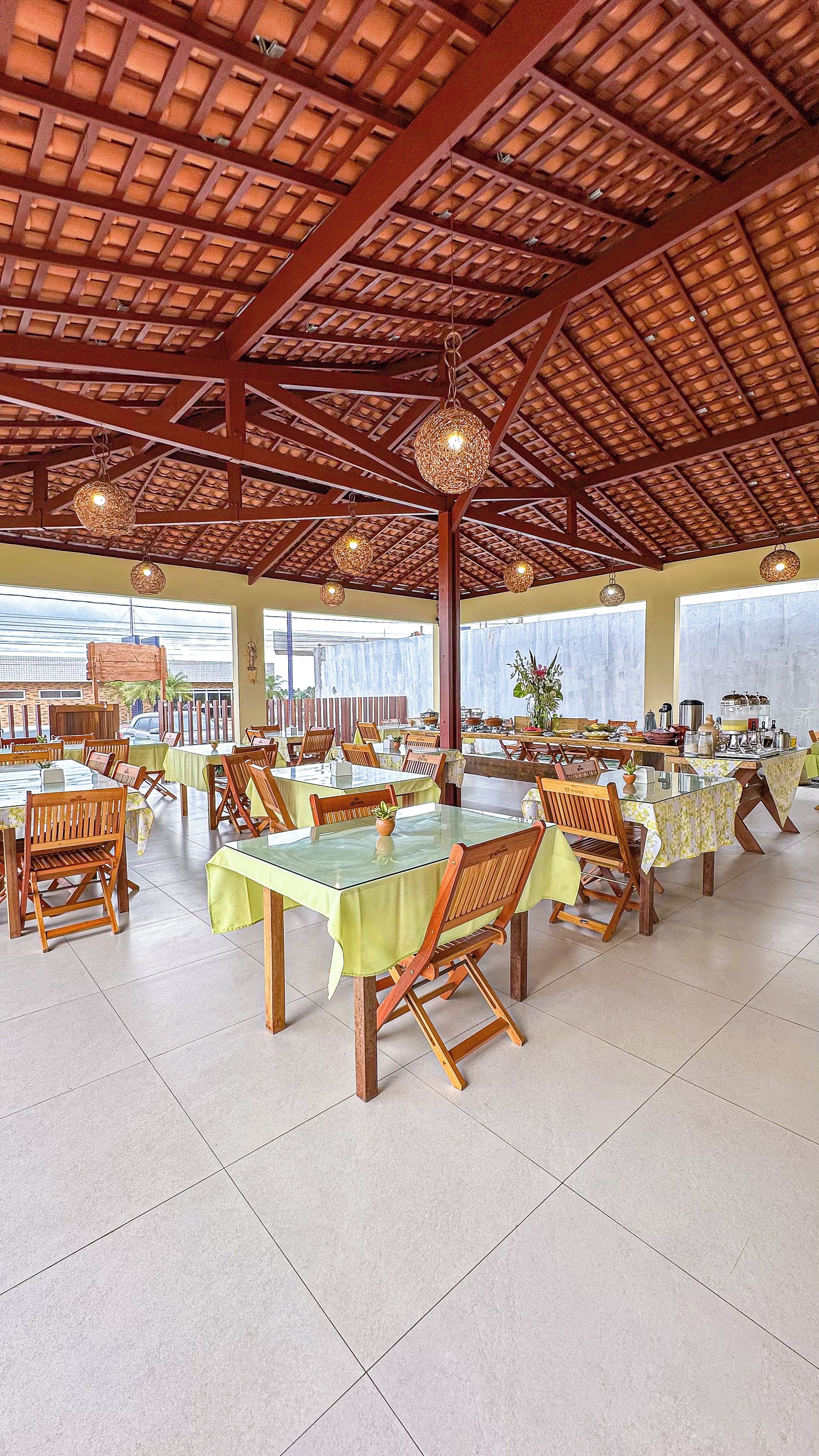 A spacious dining area with multiple tables and chairs, a high ceiling with wooden beams, and large windows allowing natural light.