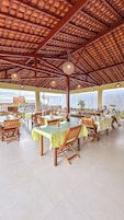 Un comedor espacioso con varias mesas y sillas, un techo alto con vigas de madera y ventanas grandes que dejan entrar luz natural.