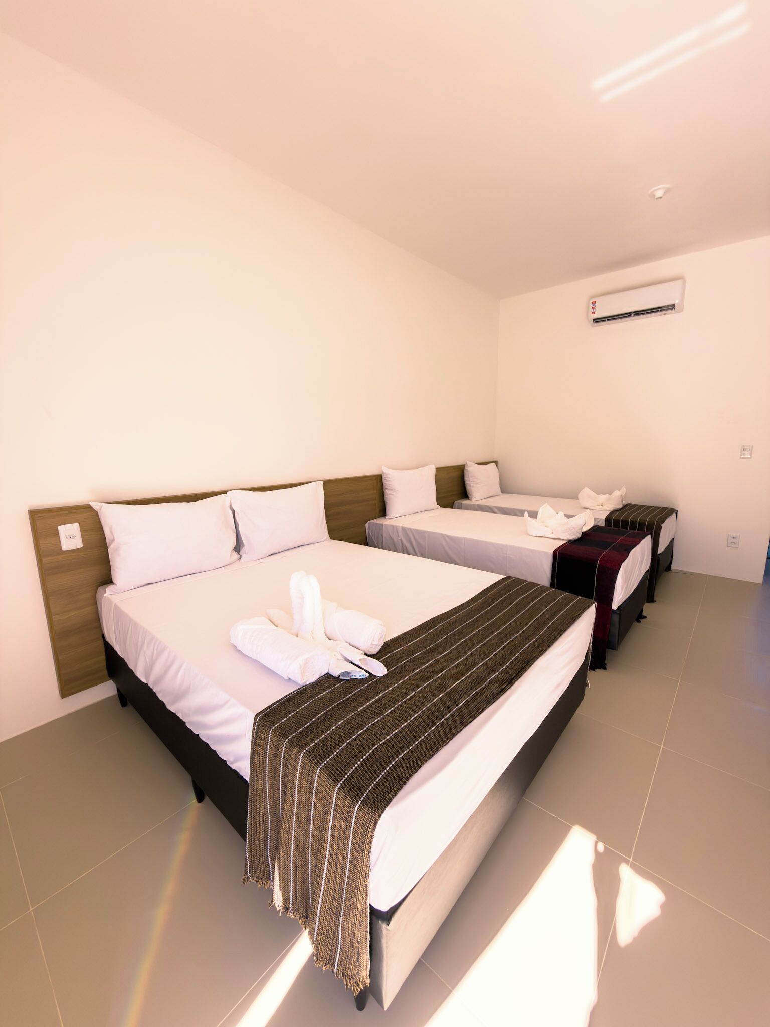 A hotel room with two beds, a wooden headboard, a striped blanket, and an air conditioning unit.