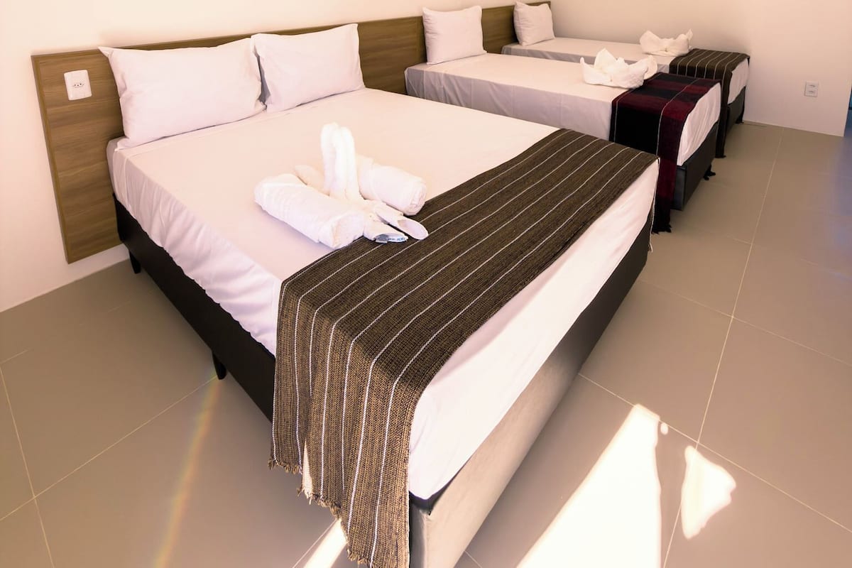 A hotel room with two beds, a wooden headboard, a striped blanket, and an air conditioning unit.