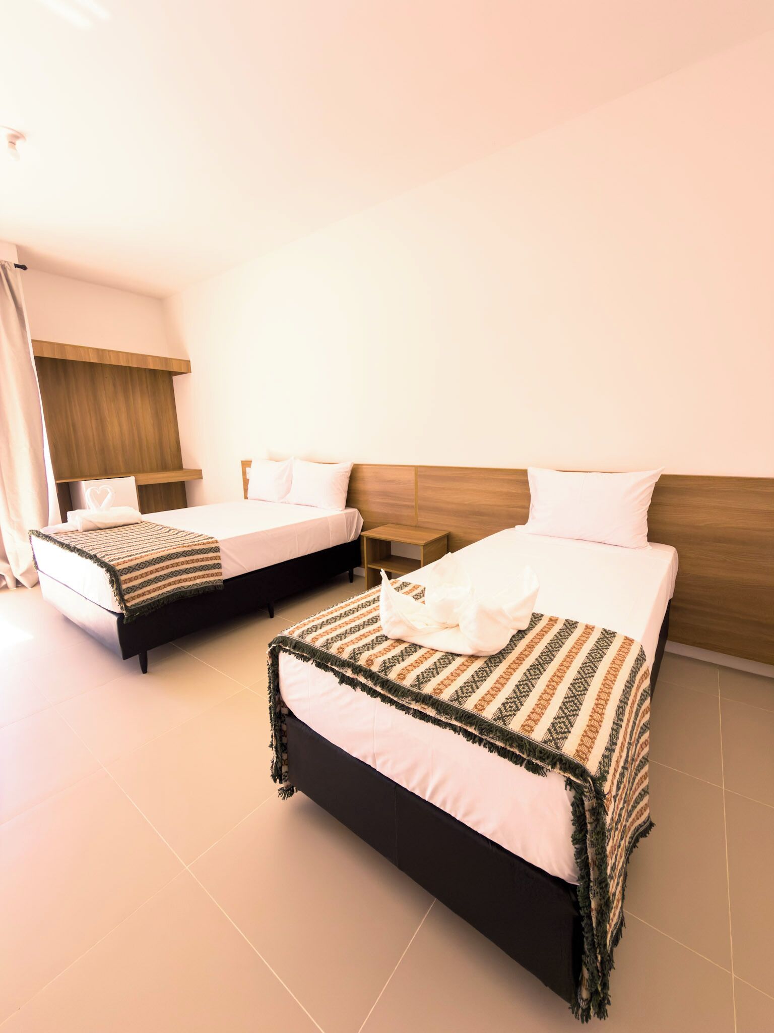 A hotel room with two beds, a wooden headboard, a bedside table, and a nightstand.