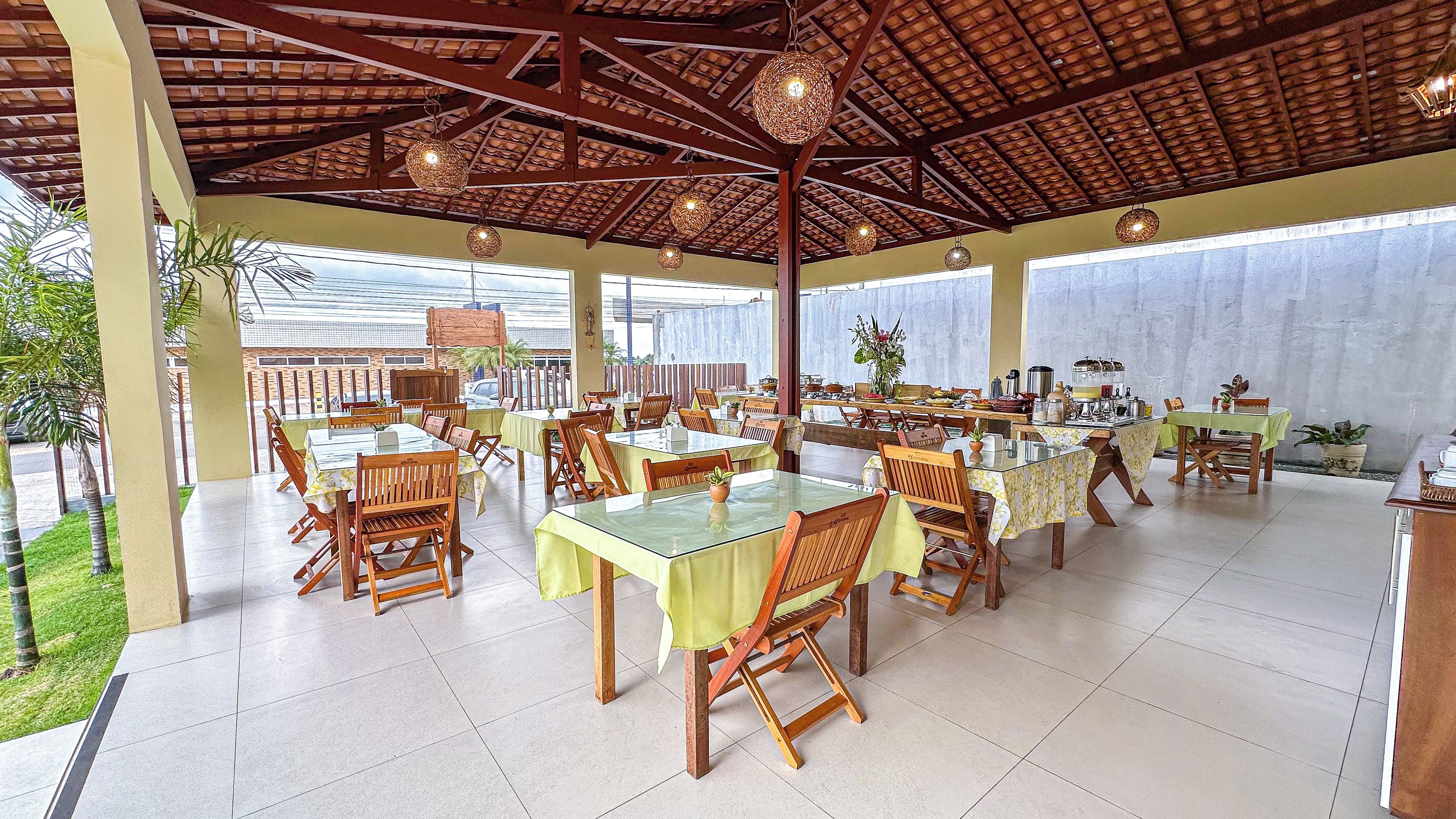 An outdoor dining area with multiple tables and chairs, a tiled floor, and a wooden ceiling structure.