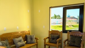 Habitación con sofá, sillas, una mesa de centro de madera, lámpara colgante y ventana con vistas a una piscina y sombrillas.
