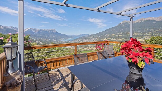 A deck with a table and chairs, overlooking a mountainous landscape.