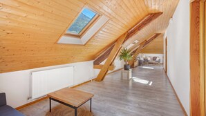 A spacious loft bedroom with a sloped ceiling, a skylight, a wooden floor, a small table, and a sofa.