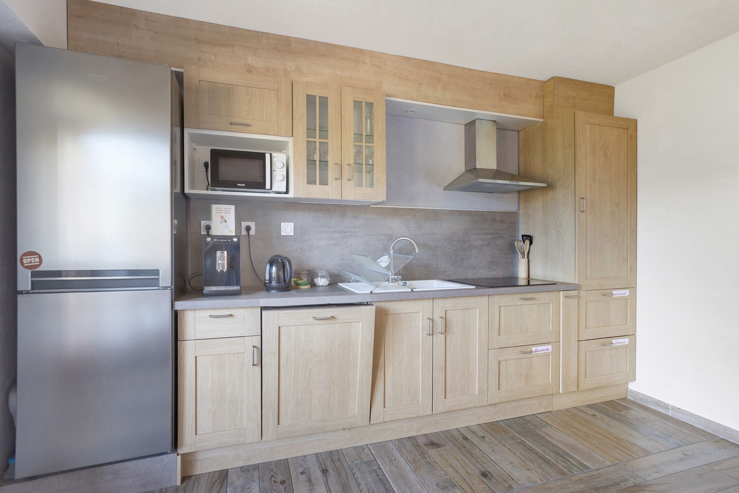 A modern kitchen with a stainless steel refrigerator, wooden cabinets, a microwave, and a stainless steel range hood.