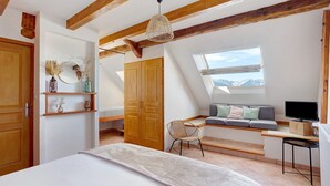 A bedroom with a bed, a desk, a chair, a TV, a window with a view, and a wooden ceiling.