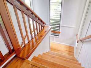 A wooden staircase with a handrail, leading to a landing with a window. - Princeville, Mauna Kai Princeville, Spacious 5 BR, Ocean View, Sleeps 14 (Princeville)