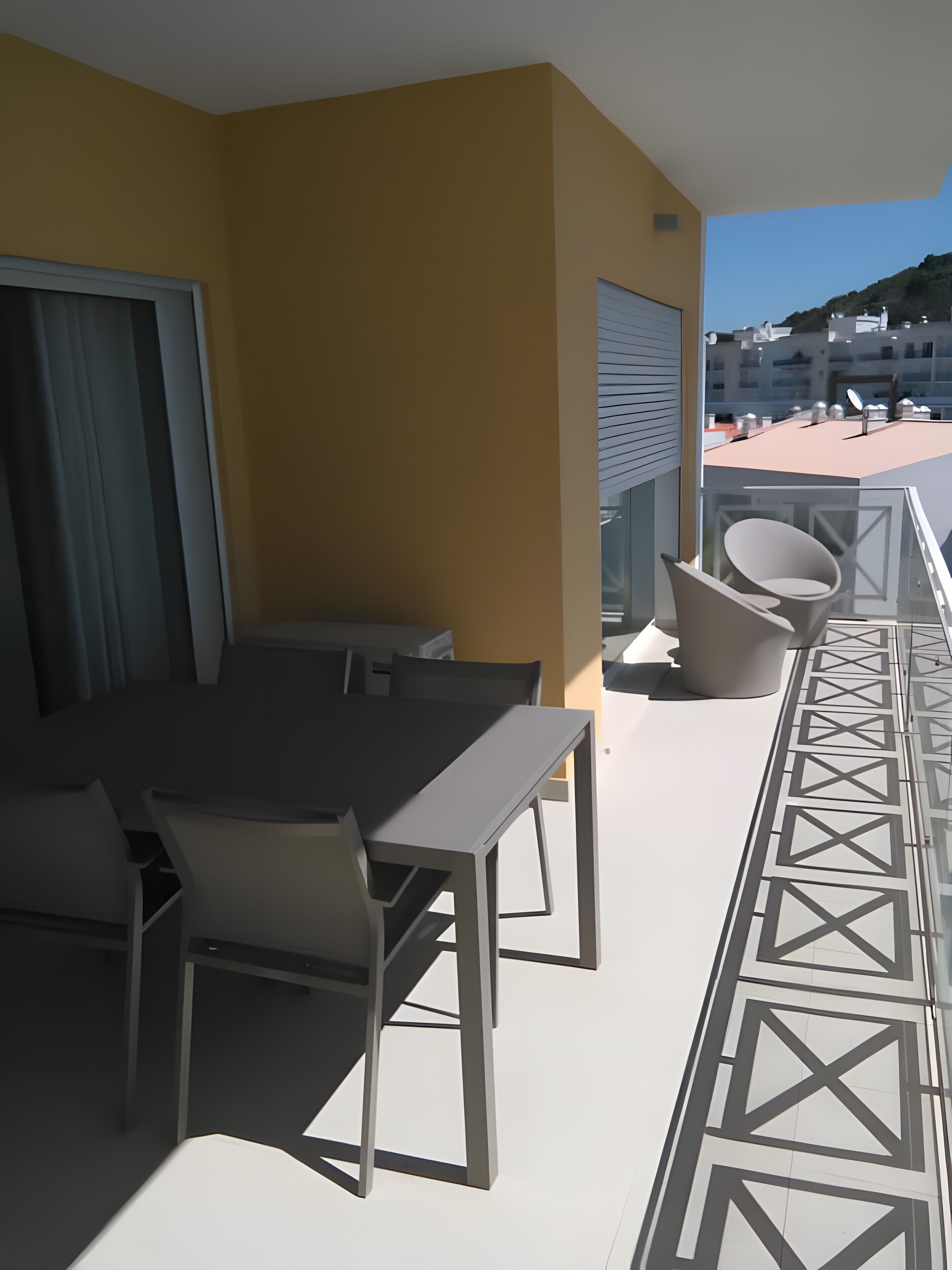 A balcony with a dining table and chairs, a patterned floor, and a view of buildings and hills.