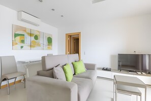 A modern living room with a sofa, a TV, and a painting on the wall. - 'T1 Garden Hill' Apartment with Shared Pool, Wi-Fi, and Air Conditioning (Albufeira)