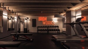Ein Fitnessstudio mit Laufbändern, Kraftgeräten und einem Neon-Schild mit der Aufschrift 'IRON WORKS'.