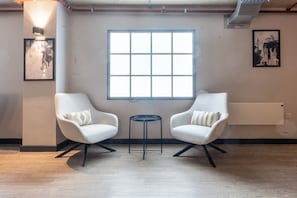 A room with two white armchairs, a small round table, a large window, and artwork on the walls. - Iron Yard (Sheffield)