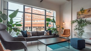 Ein modernes Wohnzimmer mit einer Couch, Sesseln, einem Couchtisch, großen Fenstern und Zimmerpflanzen.