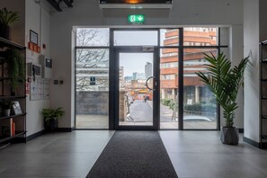 A hotel entrance with a glass door, a green exit sign, a potted plant, and a tiled floor. - Iron Yard (Sheffield)