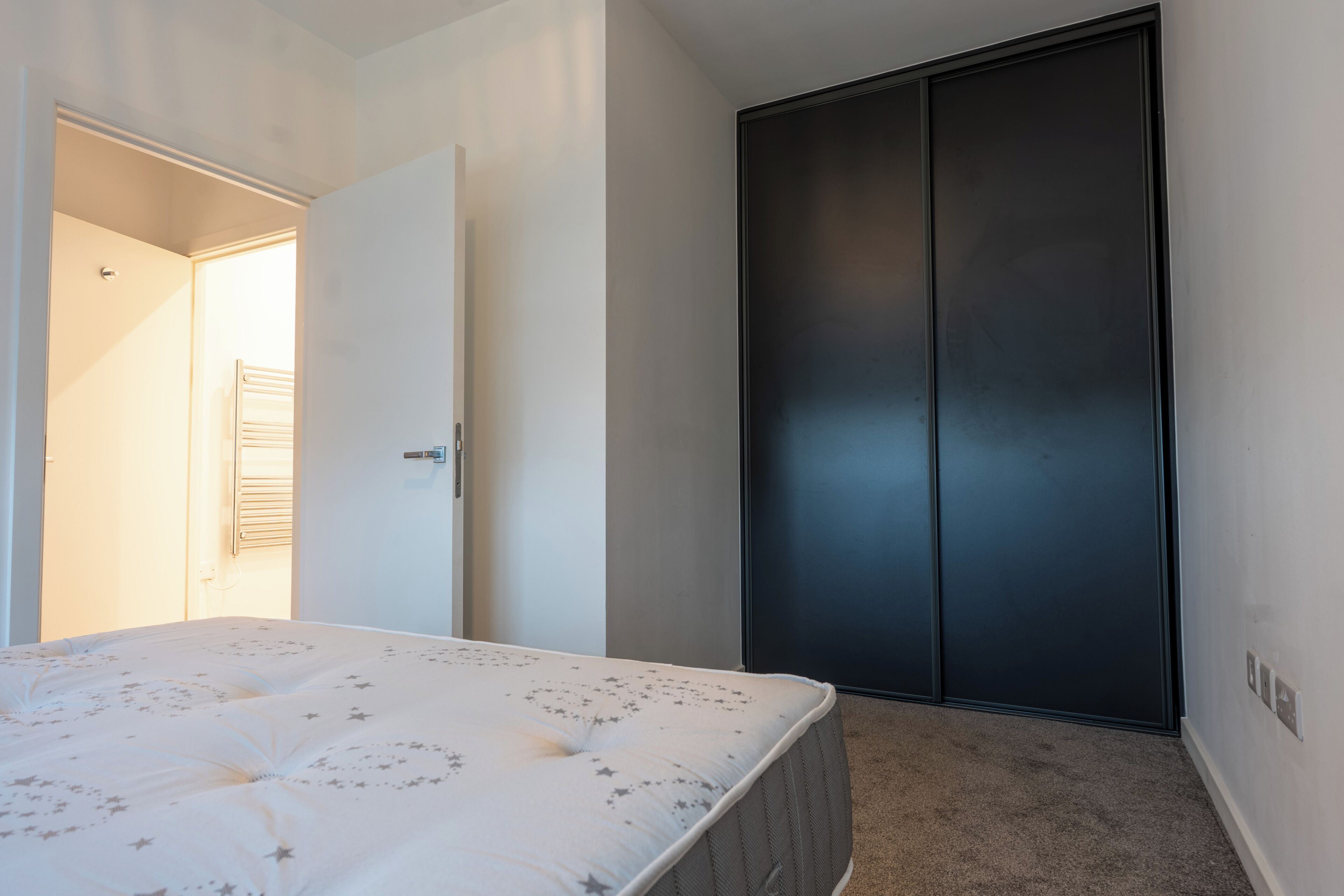 A bedroom with a bed, a wardrobe, and a door leading to another room.